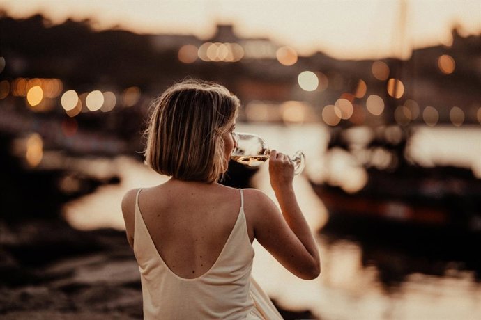 Archivo - Mujer bebiendo una copa de vino al atardecer en verano en el muelle.