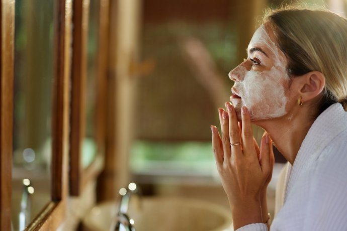 Mujer aplicándose una crema facial en el baño.