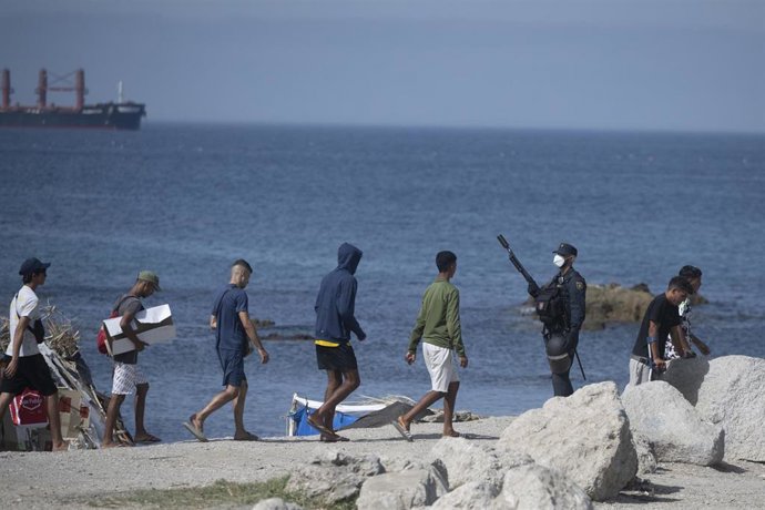 Varias personas inmigrantes circulan por la playa del Trampolín, en Ceuta.
