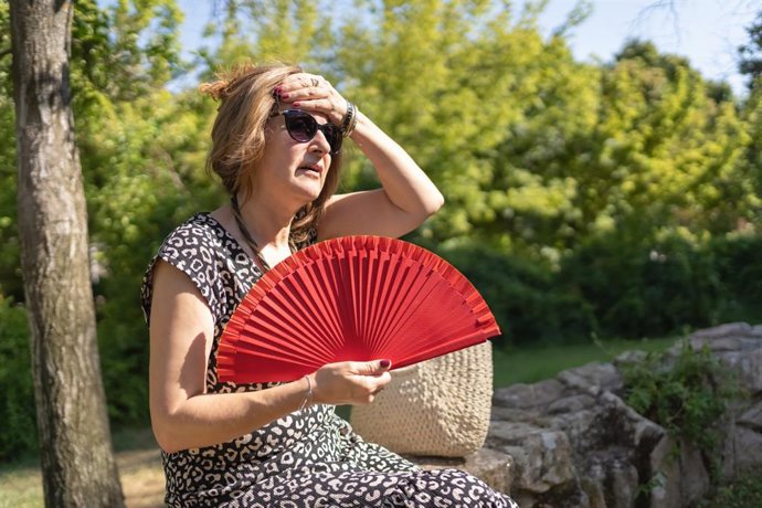 Archivo - Mujer dándose aire con un abanico en plena ola de calor en un parque.