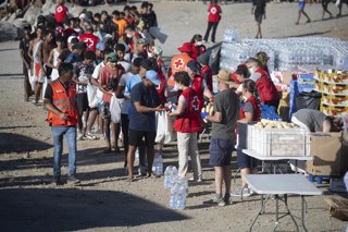 Miembros de la Cruz Roja reparten comida a los inmigrantes en una playa, a 21 de agosto de 2026, en Ceuta (España). Ceuta sigue afrontando una grave crisis humanitaria después de la histórica entrada masiva de más de 70.000 migrantes a nado por el Tarajal