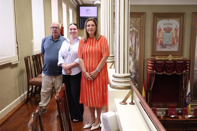 La presidenta del Parlamento de Canarias, Astrid Pérez (d), posa con el escudo de fondo