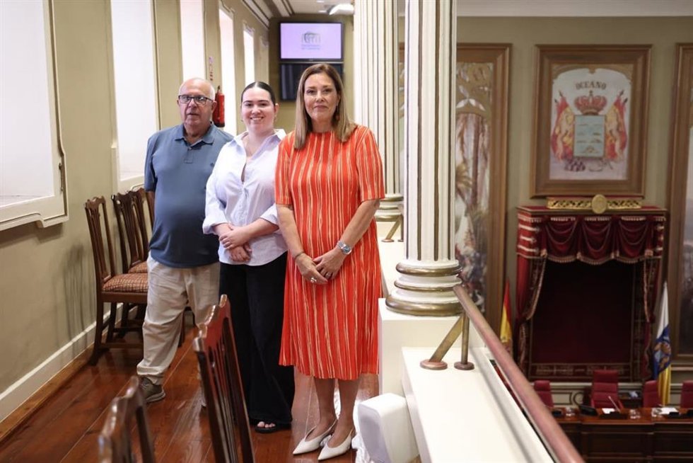 La presidenta del Parlamento de Canarias, Astrid Pérez (d), posa con el escudo de fondo