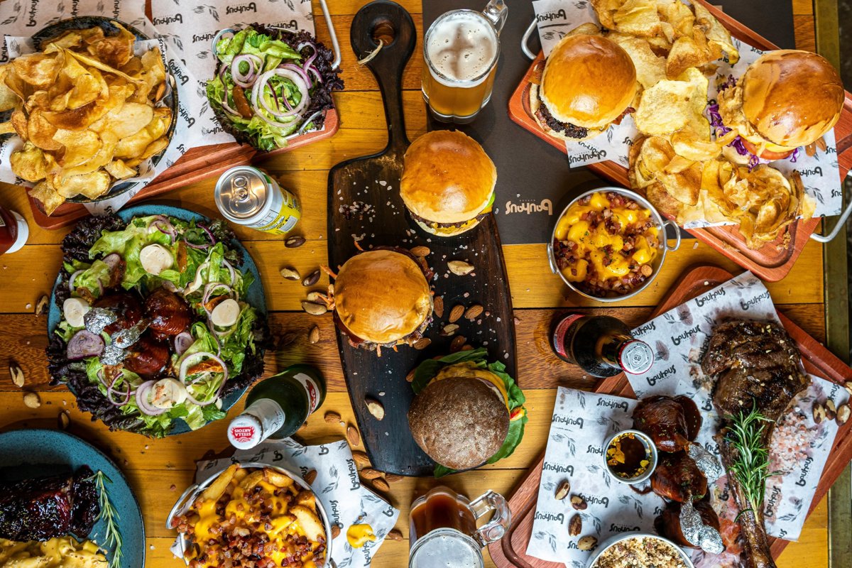 Mesa con hamburguesas, patatas, ensaladas y cerveza, vista desde arriba.