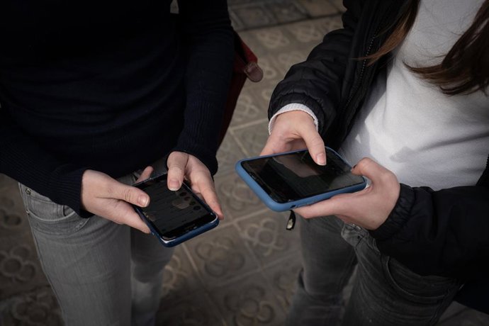 Archivo - Dues persones amb el telèfon mòbil