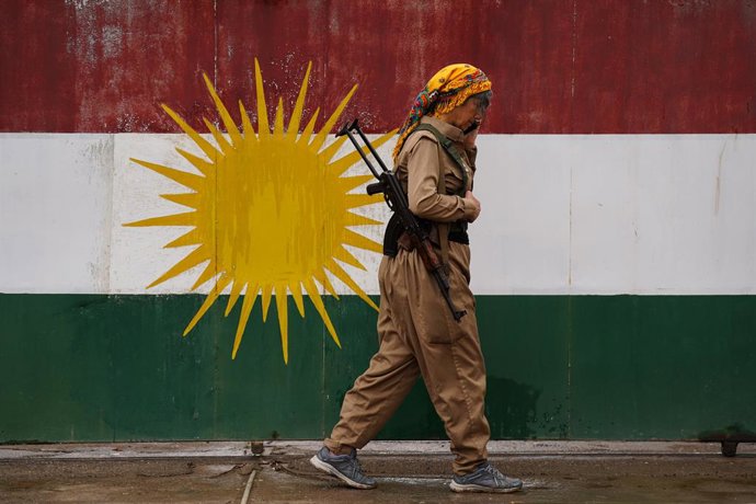 Archivo - Arquivo - 14 de março de 2026, Erbil, Iraque: Nishtman Yousefi, uma combatente curda e membro da Organização Khabat do Curdistão Iraniano (Sazmani Khabat), caminha em frente a uma bandeira curda, após um ataque com drones iranianos à base do gru