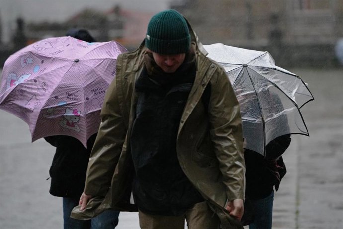 Archivo - Varias personas intentan sujetar sus paraguas bajo la lluvia