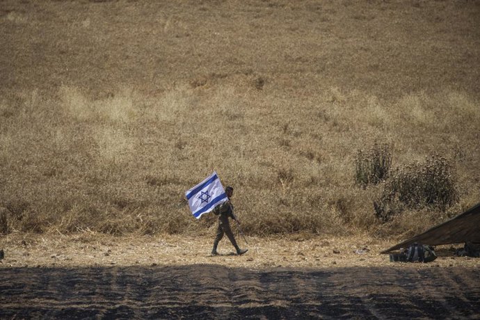 Archivo - Arquivo - 14 de maio de 2021, Israel, Sderot: Um soldado das Forças de Defesa de Israel (IDF) caminha com a bandeira israelense na fronteira de Israel com a Faixa de Gaza, perto de Sderot, em meio à escalada da violência entre israelenses e pale