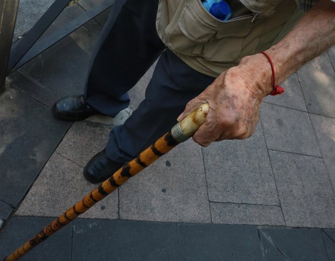 Archivo - Una persona mayor caminando por la calle con ayuda de un bastón.
