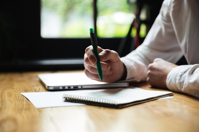 Archivo - Cropped photo of mans hand holding green pen, while taking notes