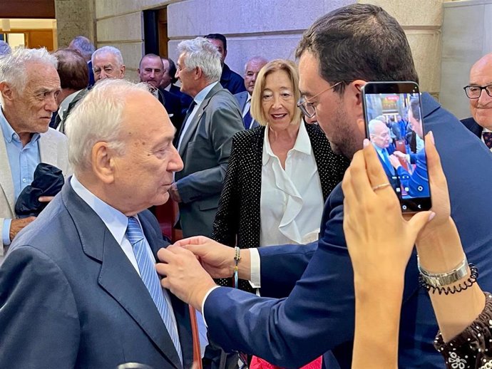 El presidente del Principado, Adrián Barbón, coloca la distinción al presidente de Industrias Lácteas Asturianas (Ilas-Reny Picot), Francisco Rodríguez.