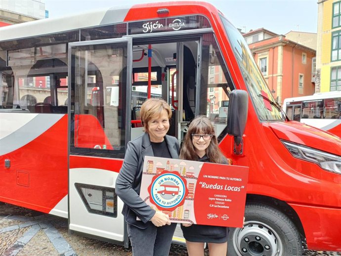 La alcaldesa gijonesa, Carmen Moriyón, desvela, junto a una alumna del colegio público Escuelona, el nombre de uno de los tres microbuses de la nueva línea en zona rural de Emtusa.