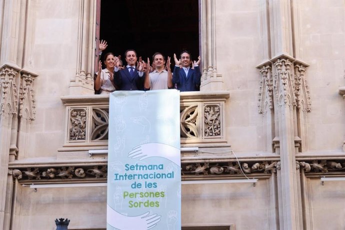El presidente del Consell de Mallorca, Llorenç Galmés, cuelga la banderola conmemorativa de la Semana Internacional de las Personas Sordas en la fachada de la sede de la institución insular mientras da un aplauso en lengua de signos.