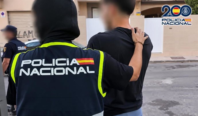 Un agente de la Policía Nacional acompaña a uno de los detenidos en la operación 'Candela', desarrollada en Roquetas de Mar (Almería).