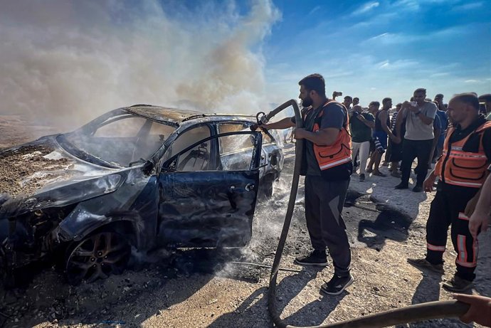 24 de setembro de 2026, Cidade de Gaza, Faixa de Gaza, Território Palestino: Chamas e fumaça se elevam de um veículo após ele ter sido atingido por um míssil israelense, enquanto equipes da Defesa Civil tentam extinguir o incêndio na rua al-Rashid, a sudo