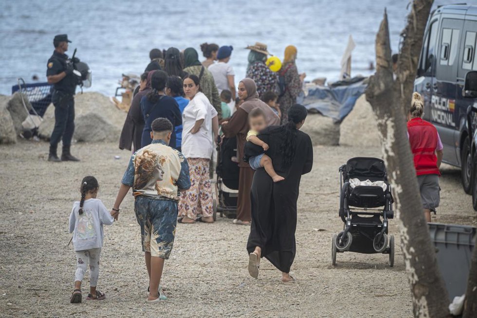 Varios migrantes recogen comida y bebida de Cruz Roja en la playa del Trampolín, a 23 de septiembre de 2026, en Ceuta (España). Embarcaciones de Salvamento Marítimo han trabajado este miércoles en la reparación de desperfectos detectados en la barrera neu