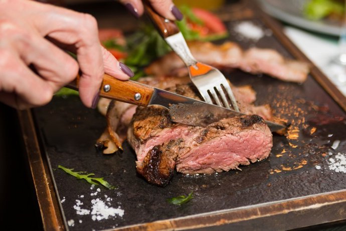 Archivo - Woman hand holding knife and fork cutting grilled beef steak