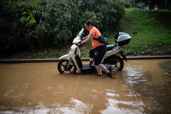 Una dona arrossega una moto en un carrer inundat de Barcelona