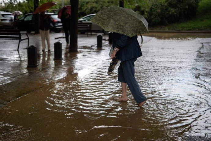 Una mujer cruza a través de la lluvia acumulada en una calle en Barcelona. 