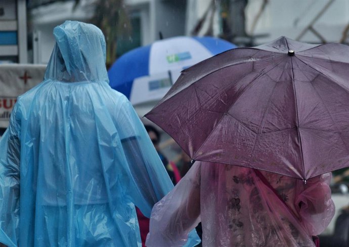 Dos personas con paraguas y chubasqueros pasen por la calle en un día de lluvias y tormentas.