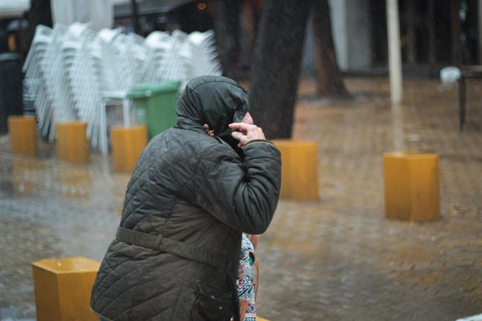 Archivo - Un viandante se protege de la lluvia con una capucha.