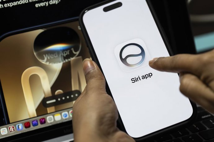 Archivo - June 10, 2026: In this photo illustration, a person holds a smartphone displaying the Siri app logo in front of a laptop screen showing an iPhone interface on June 10, 2026, in New Delhi, India.