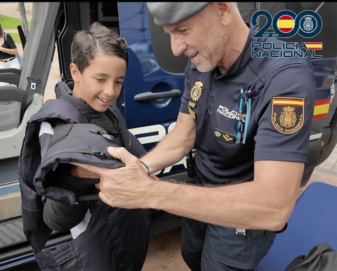 Un agente de la Policía Nacional le muestra a un niño como ponerse un chaleco en una jornada de puertas abiertas por el Día de la Policía