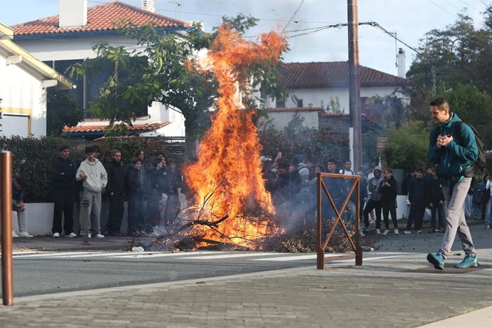 October 8, 2026, Anglet, Nouvelle Aquitaine, France: Flames rise from a large pile of burning branches on a residential street near the Cantau high school in Anglet, southwestern France, as dozens of students watch from the pavement and a man walks past i