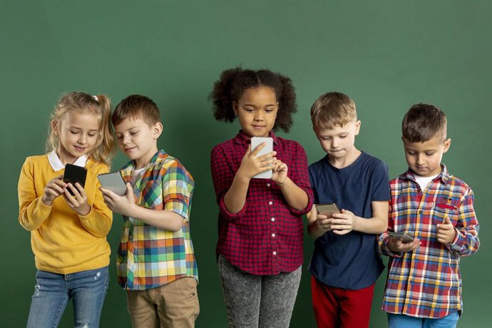 Archivo - Un grupo de niños utilizando teléfonos móviles.