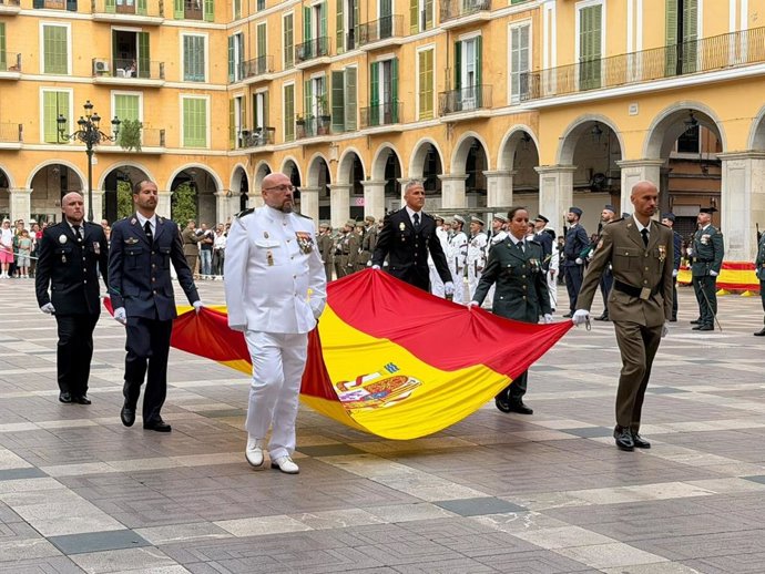 Militares de los distintos ejércitos portan la bandera española en la plaza Mayor, en Palma.