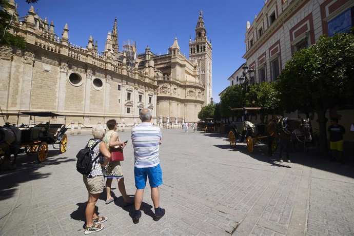 Archivo - Tres turistas miran atentamente la Giralda desde la plaza del Triunfo, a 21 de junio de 2022 en Sevilla (Andalucía, España)