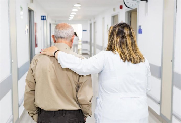 Archivo - Un profesional sanitario acompaña a una persona mayor en un hospital