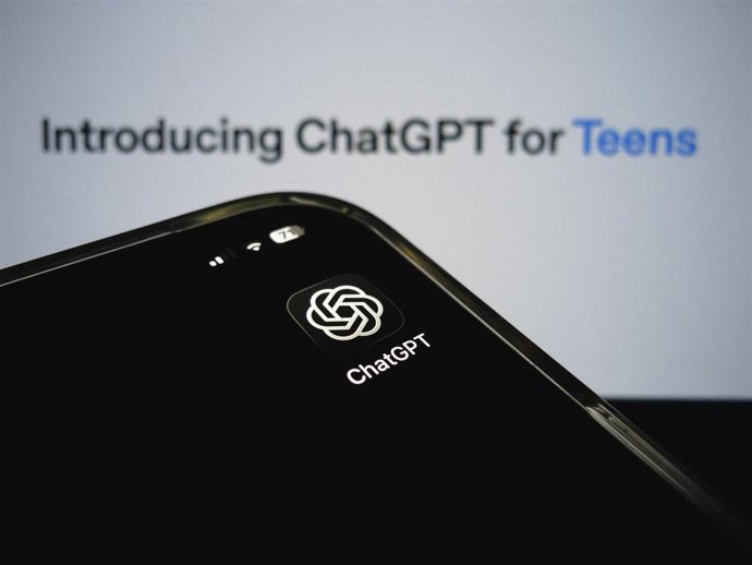 Archivo - Composición con el icono de la aplicación ChatGPT en un smartphone, al frente, con el banner de presentación de "ChatGPT para adolescentes" de OpenAI como fondo