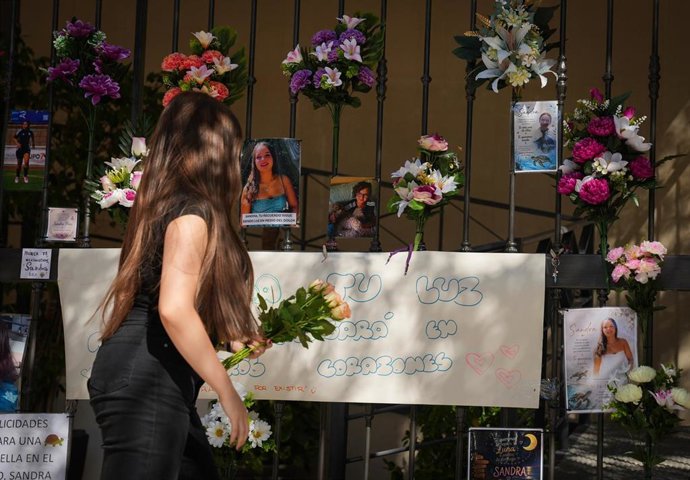Una joven pasa junto al altar en memoria de Sandra Peña, que ha sido repuesto en las rejas del bloque de viviendas de la calle Rafael Laffón 