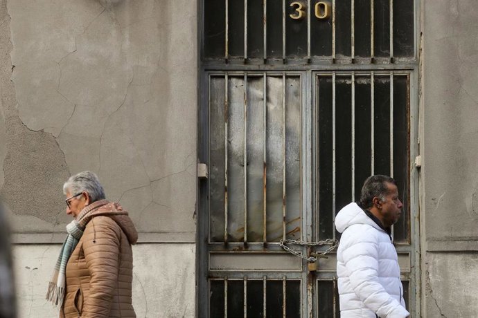 Archivo - Dos personas caminan junto a una vivienda vacía.