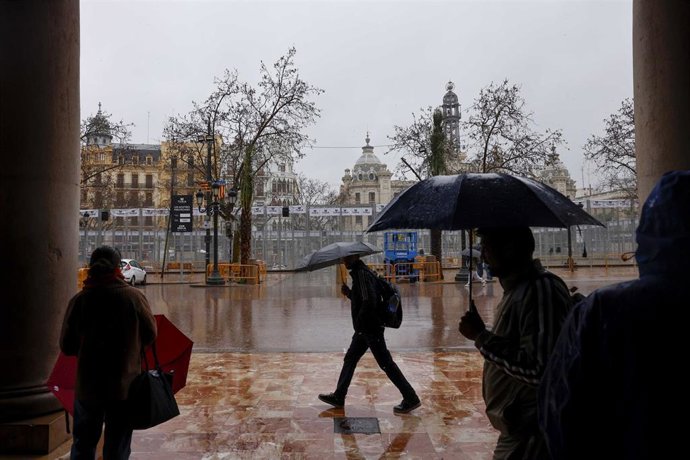 Archivo - Personas caminan bajo la lluvia durante el montaje de las Fallas 2026, en la plaza del Ayuntamiento, a 5 de marzo de 2026, en Valencia, Comunidad Valenciana (España).