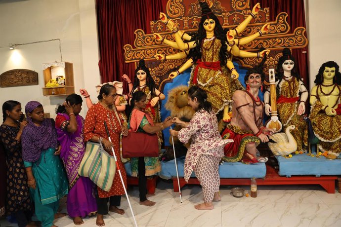 October 11, 2026, Kolkata, West Bengal, India: A sighted woman from the Banerjee family helps a blind woman touch a Durga idol, allowing her to experience the shape and features of Goddess Durga, during the family's 15-year-old Banerjee family's Durga Puj