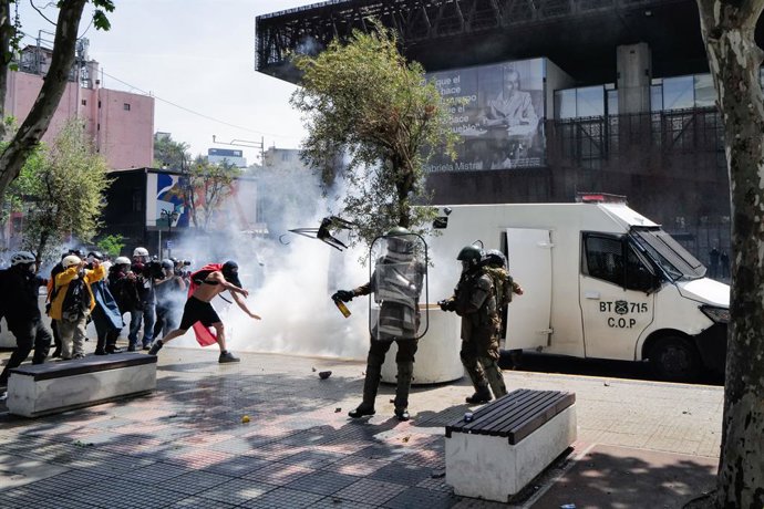 18 de outubro de 2026, Santiago, CL: SANTIAGO, CHILE – 18 DE OUTUBRO DE 2026: Uma pessoa com o rosto coberto é vista perto de policiais da Carabineros e de um veículo blindado da polícia em meio a uma nuvem branca do lado de fora do GAM, durante o sétimo 
