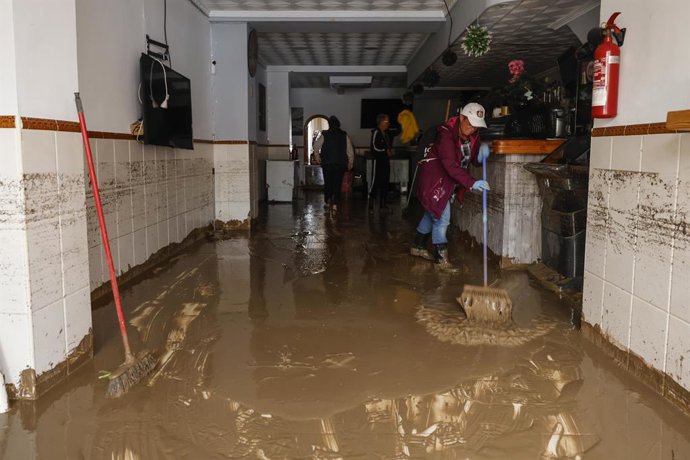 Diverses persones lleven el fang dels carrers mentre s'acumula el mobiliari que han hagut de traure a causa de les inundacions per les fortes pluges, a 19 d'octubre del 2026, als Poblets (Alacant)