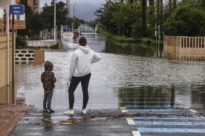 Una mujer y un niño observan una zona inundada, a 19 de octubre de 2026, en Guardamar de la Safor, Valencia, Comunidad Valenciana (España). La Generalitat Valenciana prepara una orden de confinamiento para el litoral sur de Valencia y el litoral norte de 