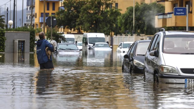 Un hombre atraviesa con un perro una zona inundada, a 19 de octubre de 2026, en Guardamar de la Safor, Valencia, Comunidad Valenciana (España).