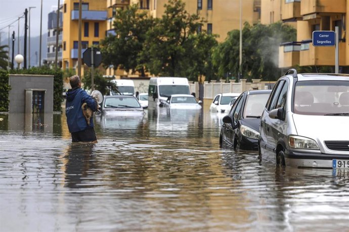 Un hombre atraviesa con un perro una zona inundada, a 19 de octubre de 2026, en Guardamar de la Safor, Valencia, Comunidad Valenciana (España). 