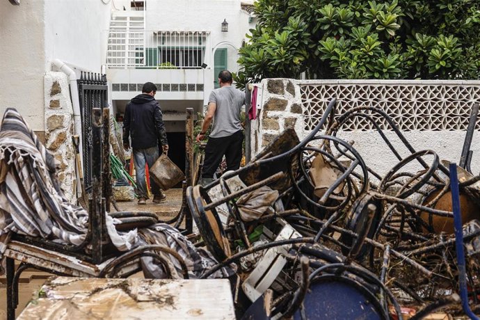 Varias personas quitan el barro de las calles mientras se acumula el mobiliario que han tenido que sacar debido a las inundaciones por las fuertes lluvias, a 19 de octubre de 2026, en Els Poblets (Alicante)