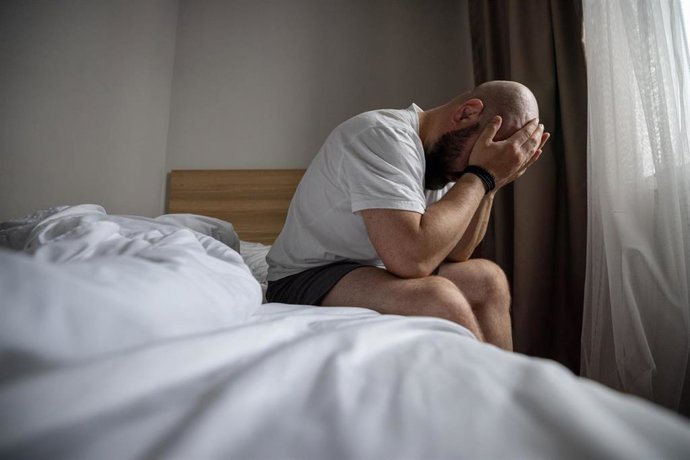 Archivo - Hombre sentado en la cama sujetándose la cabeza en una mañana penumbra en el dormitorio. Estrés, depresión, soledad