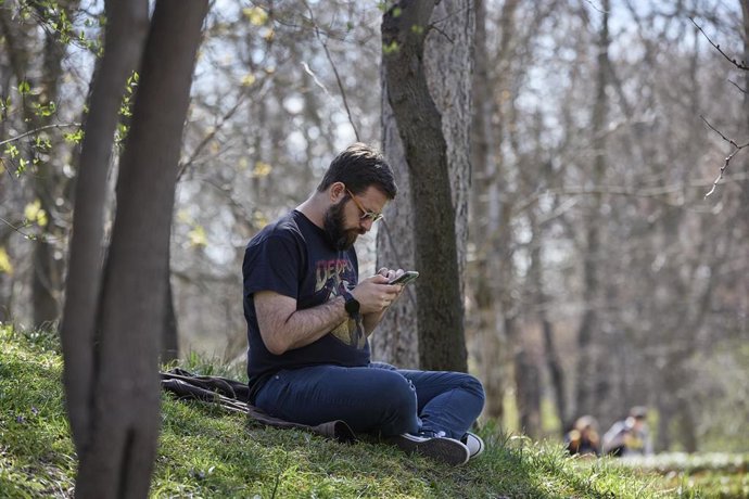 Archivo - Un hombre mira su teléfono móvil en el Parque del Retiro, a 11 de marzo de 2023, en Madrid (España). La masa de aire de este fin de semana sobre España procede del océano Atlántico de latitudes inferiores a los 30ºN. Esta masa de aire cálida, un