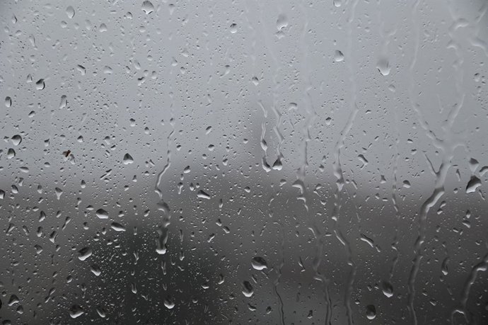 19 de outubro de 2026, Marselha, França: Uma imagem de gotas de chuva e fios de água escorrendo por uma vidraça transparente, tendo como pano de fundo um cenário sombrio em um dia chuvoso.