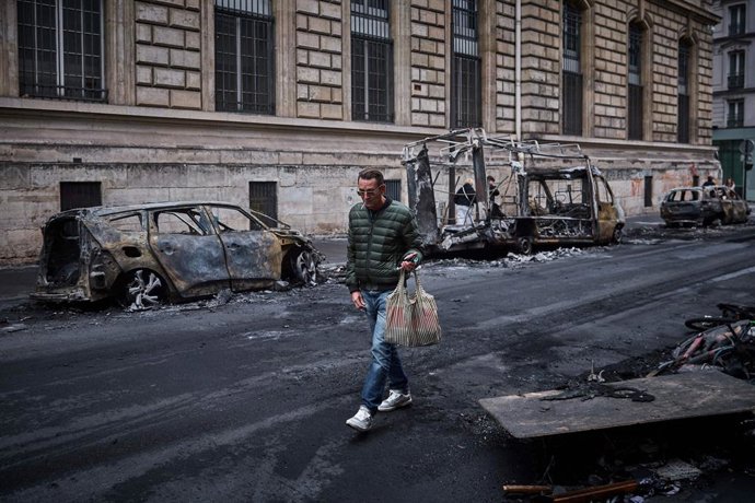 19 October 2026, France, Paris: A man walks past burnt-out vehicles on Rue Yves Toudic in central Paris, France, following nationwide protests over the high cost of living. On 17 October, 1,200 people were arrested and 150 police officers were injured in 