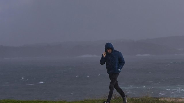 Archivo - Un hombre se protege del viento y la lluvia
