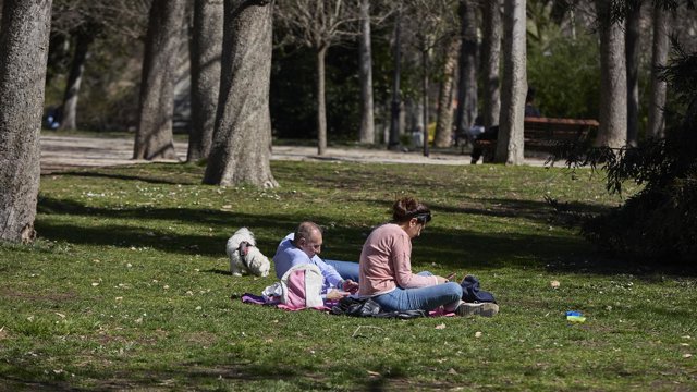Archivo - Una pareja y su perro sentados en el césped aprovechando la subida de las temperaturas en el Parque del Retiro, en Madrid.