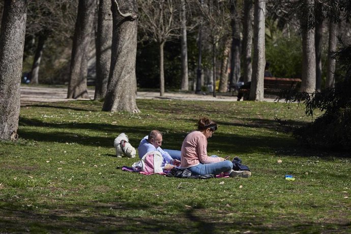 Archivo - Una pareja y su perro sentados en el césped aprovechando la subida de las temperaturas en el Parque del Retiro, en Madrid. 